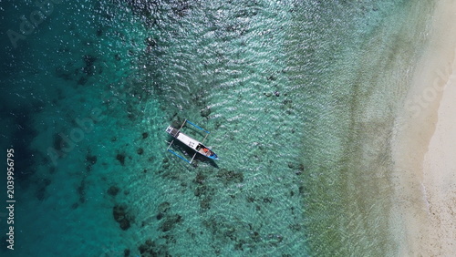 Aerial top down view of a traditional boat floating on crystal clear turquoise ocean in Lombok, Indonesia.