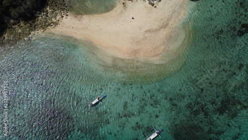 Aerial top down view of a traditional boat floating on crystal clear turquoise ocean in Lombok, Indonesia.