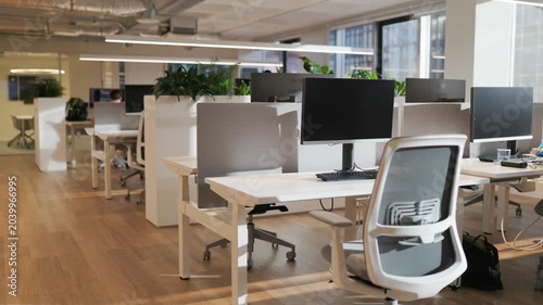 Modern office workspace with multiple desks and computers, showcasing a clean and organized environment with plants and natural light streaming through large windows