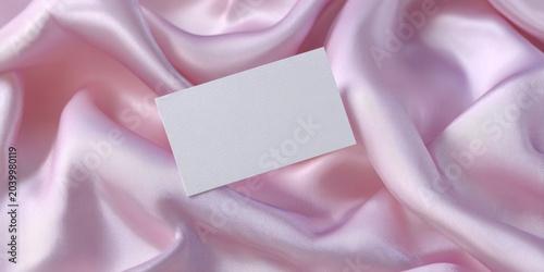 a hand in white gloves holds out an empty business card on the background of pink satin fabric