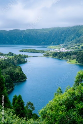 photograph of the beautiful blue lagoon with green hills and forest surrounding it. the lake is surrounded by small islands. a village sits on one side of the lake.