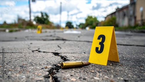 Yellow evidence marker numbered three next to a spent bullet casing on a cracked asphalt road surface.