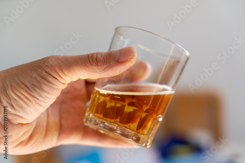 Photos Holding a glass of amber drink with ice in casual setting during afternoon