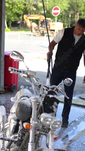 Join this motorcycle enthusiast as he washes his pride and joy at a self-service car wash. The gleaming foam and focused effort transform his bike into a stunning work of art. Vertical 4k footage.