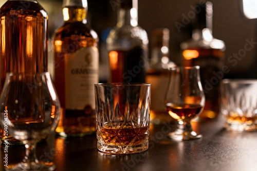 Assorted Whiskey Bottles and Glasses with Amber Liquor on Bar Counter