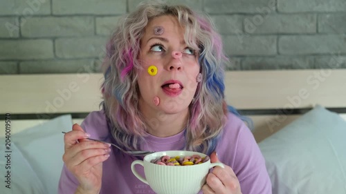 Cute cheerful woman with bright hair eats dry children's breakfast, multi-colored rings in a white plate