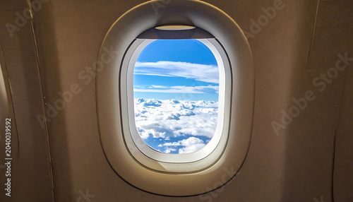 View from airplane window showing blue sky with white clouds above snow-capped mountains