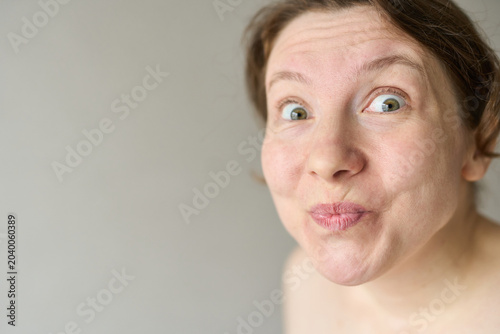 Schilderij op canvas Woman Puckering Lips And Making Playful Kiss Face In Plain Gray Background Closeup Portrait Bare Shoulders Expressive Eyes Looking At Camera