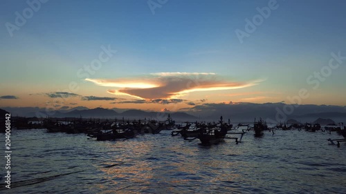 Sunrise over tropical bay with local fisherman boats silhouette, scenic golden hour sky and lenticular cloud landscape for travel video. Papuma Beach, Jember, Indonesia
