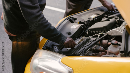 Cuadro en lienzo Mechanics inspect open hood engine bay of yellow taxi on city street