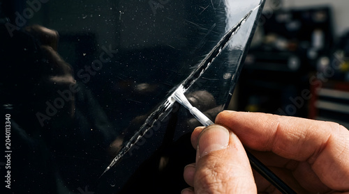 Close-up of a mechanic's hand applying white touch-up paint to a deep scratch on a dark blue car panel, professional automotive paint restoration and car body repair in a garage workshop