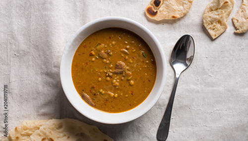 Hearty bowl of lentil soup or daal with naan bread and spoon on textured tablecloth overhead view indian food ethnic food comfort food textured background flatbread vegetarian delicious
