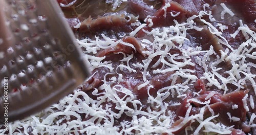 Hard cheese grated and sprinkled over beef slices, preparing beef carpaccio, close up