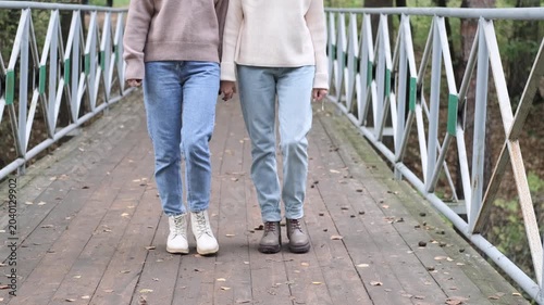 Two girlfriends are walking outside in autumn. View of the feet of two girls in autumn shoes walking along a wooden bridge in a city park.
