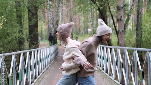 Two girlfriends are walking and having fun outside among autumn trees in a city park.