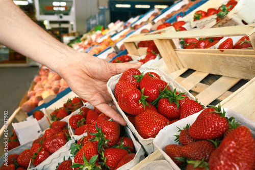 Picking ripe fruits in a grocery store: hand of a shopping customer reaching for delicious fresh strawberries