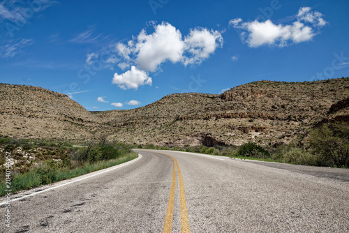 Scenic Desert Highway Winding Through Arid Hills Under a Bright Blue Sky with White Clouds