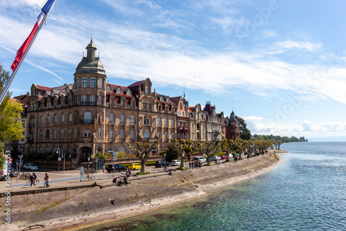 Panoramic view of Seestrasse embankment with historic architecture and people walking along Lake Constance on a bright sunny day