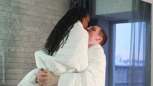 A man lifts his wife in his arms, wrapped in a warm white blanket. Happy loving couple. Beautiful wife and handsome husband enjoying a tender moment.