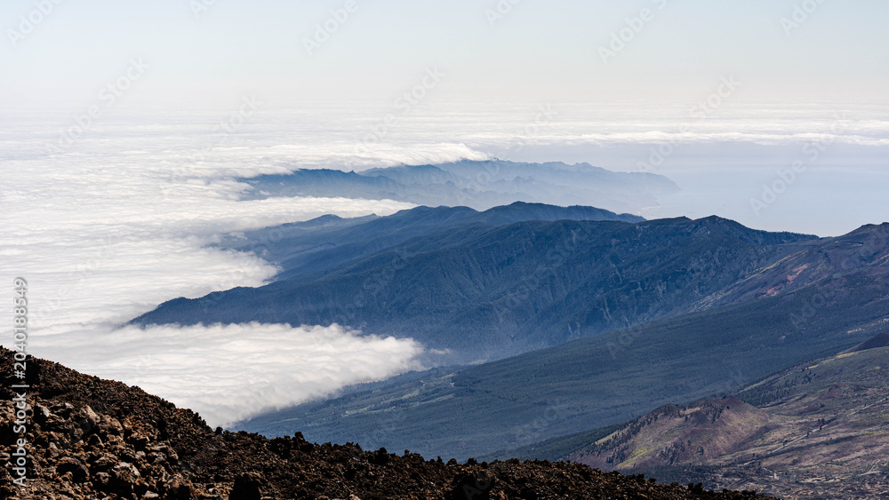 Obraz premium Stunning aerial view of a white sea of clouds rolling over pine forests and volcanic mountain ridges in Tenerife.