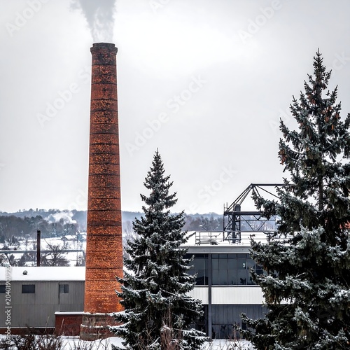 Tall brick smokestack emitting white smoke against winter sky.