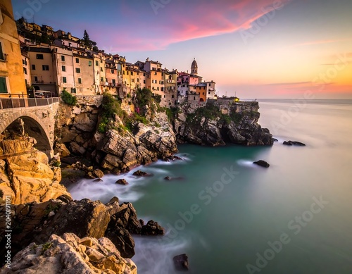 Colorful sunset over historic coastal town with rocky shore.