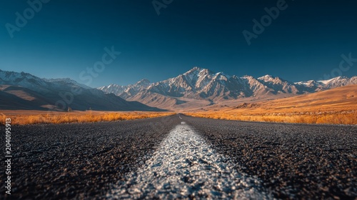 Scenic mountain road stretching towards distant peaks under a clear blue sky.