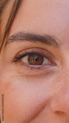 Extreme close-up macro portrait of face. Young adult beautiful pretty woman's eyes looking at camera. Brown eyes of teen lady female. Caucasian woman opening blinking eyes, smiling. Laser correction
