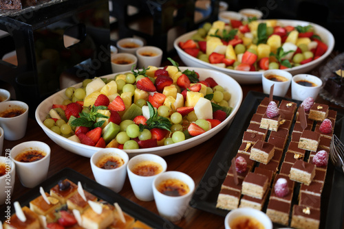 Tableau sur toile A lavish catering display featuring a colorful bowl of fresh fruit, individual crème brûlée desserts, and sophisticated chocolate petit fours