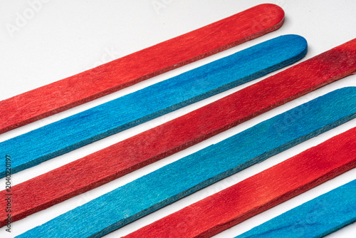Red and blue colored wooden popsicle sticks. Vibrant red and blue wooden craft sticks arranged in an alternating diagonal pattern on a clean white background. Creating a cheerful and organized feel.