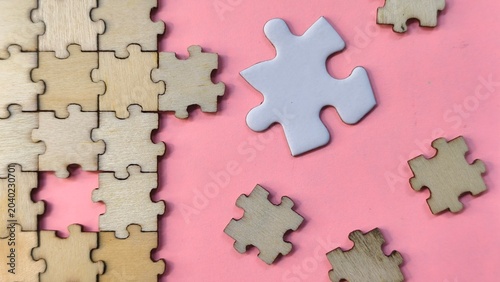 Fotografía jigsaw puzzle pieces , A single white puzzle piece among scattered wooden pieces on a pink background, representing a unique solution or a standout choice