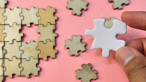 Cuadro en lienzo A single white puzzle pice among scattered wooden pieces on a pink background, representing a unique solution or a standout choice