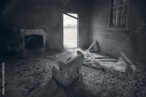 A monotone abandoned mechanics hall interior with torn armchair, fireplace and hazy countryside view, Australia