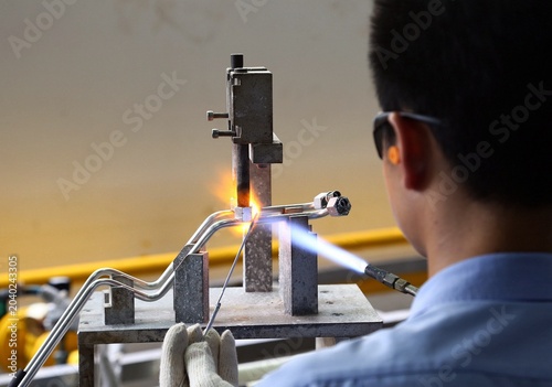 Bild auf Leinwand Shanghai, China - June 2022: A professional welder using a blowtorch to perform precision brazing on metal pipelines in a modern factory workshop, focusing on manufacturing craftsmanship