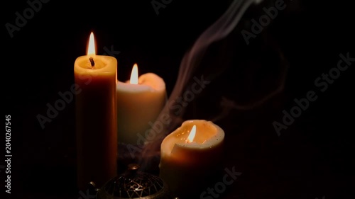 Three magic Christmas wax candle flames calm burning in home in white smoke from incense aroma stick on black dark background with copy space. Closeup yoga, spa, wellness, relaxation. No people