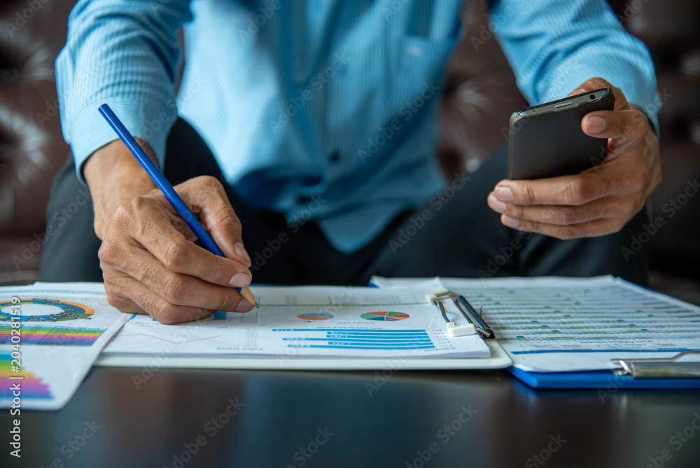 Fototapeta premium Asian Businessman reading financial spreadsheet graph chart Planning to analyze marketing data. Man reading financial graph chart Planning analyzing marketing data. Asian freelance writing paper