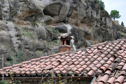 an old red tile roof and a chimney against the backdrop of a high cliff