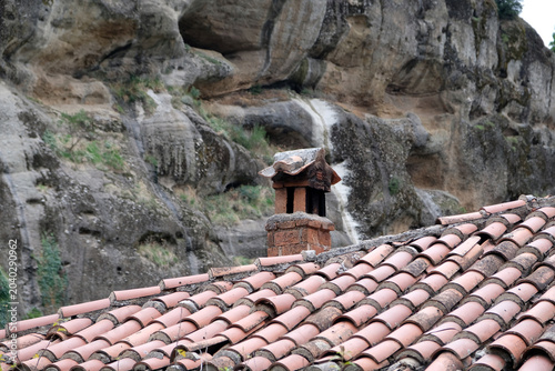 an old red tile roof and a chimney against the backdrop of a high cliff