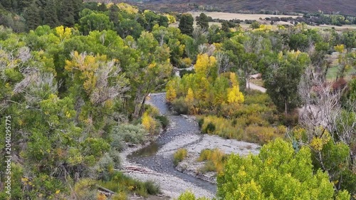Aerial view of Colorado fall landscapes featuring fall foliage trees, meandering river, and dirt road in the San Juan Mountains valley wilderness near Ridgway - 4K Drone