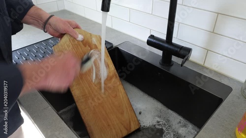 Stockholm, Sweden A man scrubs a wooden kitchen cutting board with soap and water. 