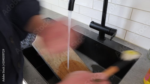 Stockholm, Sweden A man scrubs a wooden kitchen cutting board with soap and water. 