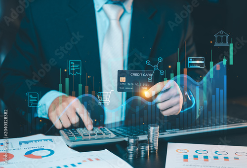Businessman holding a credit card analyzing financial stock market charts and graphs on virtual screen. Online banking and investment concept.