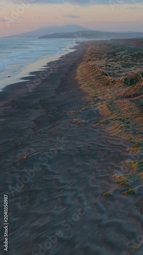 Sunset over Kawhia Beach, New Zealand. Dunes and forest meet the ocean. A surfer enjoys the waves. A peaceful scene of nature's beauty.