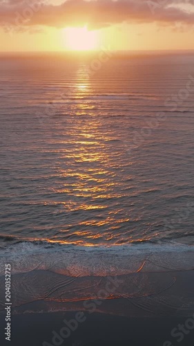 Golden hour at the beach in Kawhia, New Zealand. The sun reflects off the ocean waves as they meet the sandy shore, creating a serene coastal scene.