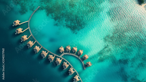 Aerial view of curved overwater villas and boardwalk above turquoise ocean lagoon
