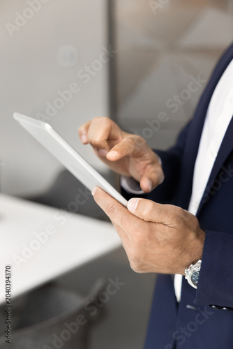 Fotografia Close up of businessman in formal suit working on digital tablet device, correspond on business e-mails, review data, making market research