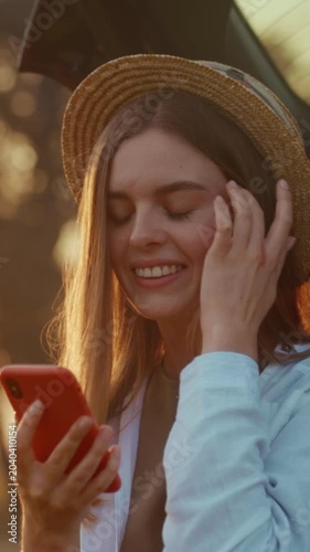 Casual woman with smartphone, Smiling woman in straw hat browsing messages outdoors during warm summer evening