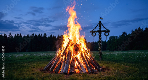 Roaring bonfire, twilight sky, midsummer pole behind with Swedish flag