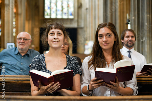 Tableau sur toile Two women holding hymnals in a church, smiling during a service.