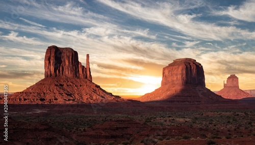 Obraz na plátne The towering buttes of Monument Valley glow in deep red as the sun sets behind them